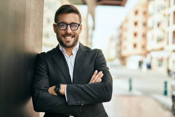Fiatal spanyol üzletember, keresztbe tett karokkal, boldogan mosolyog a városra.. - Fotó, kép