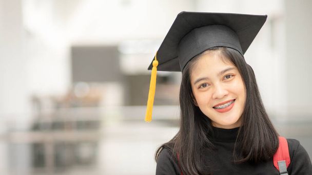 Νεαρή ευτυχισμένη Ασιάτισσα απόφοιτος πανεπιστημίου με στολή αποφοίτησης και καπέλο στο πανεπιστήμιο. Εκπαίδευση φωτογραφία αρχείου - Φωτογραφία, εικόνα