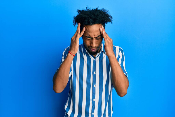 Young african american man with beard wearing casual striped shirt with hand on head for pain in head because stress. suffering migraine.  - Foto, immagini