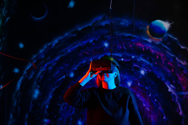 Fiatal gyönyörű vidám lány virtuális valóság szemüveg kék és piros fények a játszószobában - Fotó, kép