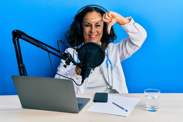 Gyönyörű középkorú orvos nő dolgozik a rádióban stúdió mosolygós, hogy keret kezek és ujjak boldog arcát. kreativitás és fényképezés koncepció.  - Fotó, kép