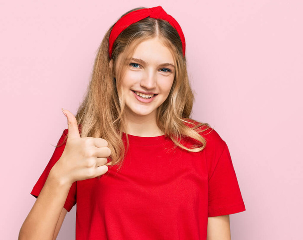 美しい若い白人の女の子が手で幸せな親指アップジェスチャーを行うカジュアルな赤いTシャツを着ています。成功を示すカメラを見ると.  - 写真・画像