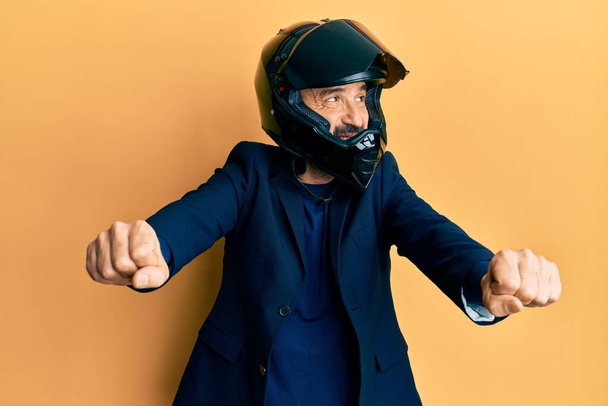 Latynos w średnim wieku, noszący kask motocyklowy, robiący symbole moto z uśmiechniętymi rękami patrzącymi w bok i myślącymi.  - Zdjęcie, obraz