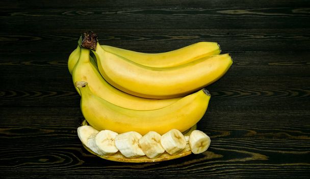 ripe slice-cut bananas on a dark wooden background - Photo, Image