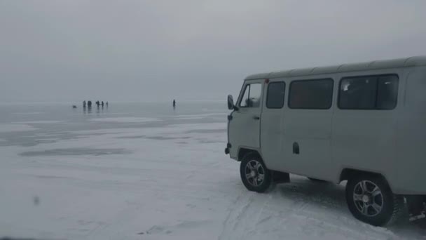 Minibus UAZ transports tourists on the frozen ice of Lake Baikal against the backdrop of groups of people and cars  - Footage, Video
