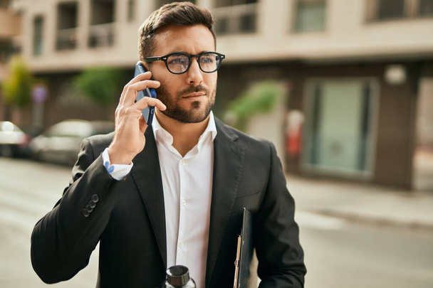 Молодий іспаномовний бізнесмен з серйозним виразом розмовляє по смартфону в місті
. - Фото, зображення
