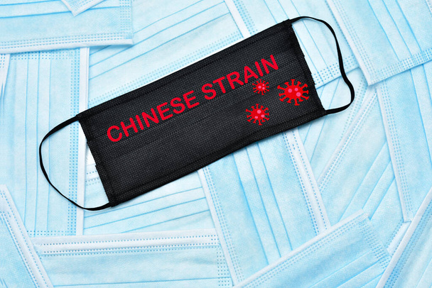 Surgical masks as background. In the center a text that says Chinese strain. Concept of the coronavirus pandemic and its variants. - Photo, Image