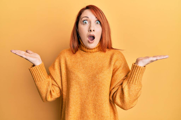 Beautiful redhead woman presenting with open palm afraid and shocked with surprise and amazed expression, fear and excited face.  - Foto, imagen