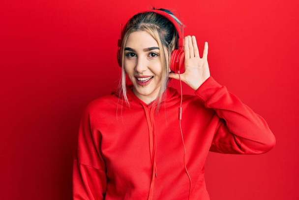 Young modern girl wearing gym clothes and using headphones smiling with hand over ear listening an hearing to rumor or gossip. deafness concept.  - Photo, Image