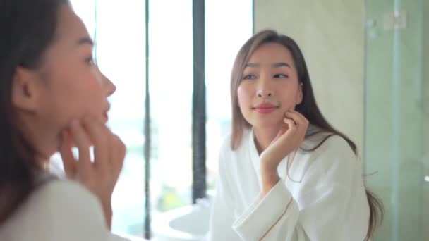 Ritratto bella giovane donna asiatica applicare cosmetici da specchio di bagno interno - Filmati, video
