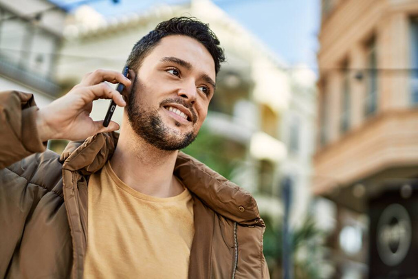 Молодий іспаномовний чоловік посміхається щасливим розмовляти по смартфону в місті
. - Фото, зображення