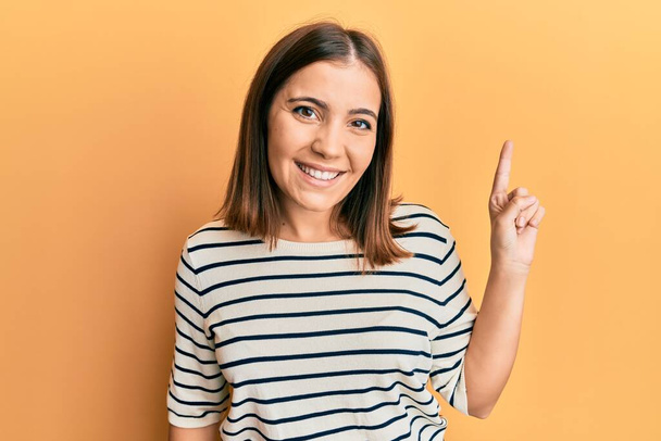 Jonge mooie vrouw draagt casual gestreepte t-shirt glimlachen met een idee of vraag wijzend vinger omhoog met gelukkig gezicht, nummer een  - Foto, afbeelding