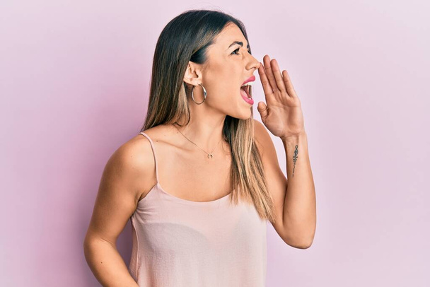 Young hispanic woman wearing casual sleeveless t shirt shouting and screaming loud to side with hand on mouth. communication concept.  - Photo, Image