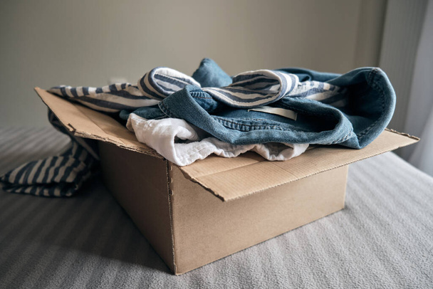 Cardboard box with pre owned clothes inside. Sustainable fashion, resale used clothes - Fotografie, Obrázek
