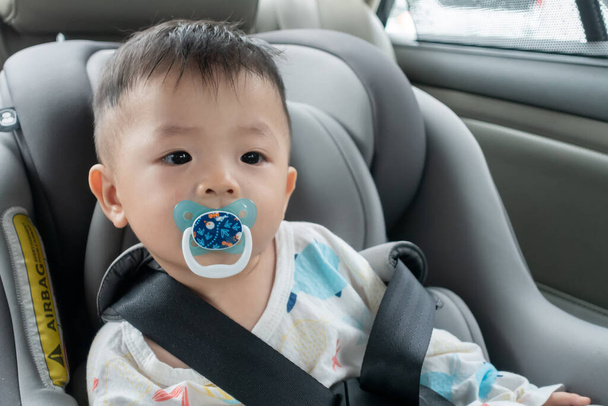 Stile di vita locale asiatico bambino cinese con faccia emotiva e succhiare ciuccio mentre sedersi sul seggiolino auto di sicurezza per bambini - Foto, immagini