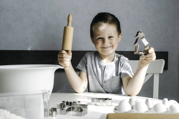 Mały chłopiec przygotowuje ciasteczka w kuchni i trzyma wałek w rękach. Gotowanie deserów z dziećmi. Rodzinne zajęcia. Prawdziwe autentyczne chwile z życia - Zdjęcie, obraz