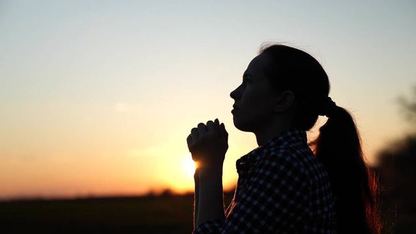日没の終わりに祈るクリスチャンの女性。家族や子供たちへの太陽の祈りの光の中で空の背景に女の子。自然の中でのリラクゼーションと瞑想,健康的なライフスタイル - 写真・画像