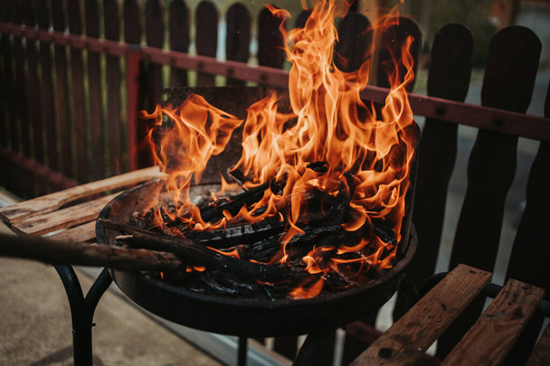 A branch poking and feeding a fire on a fire pit next to a wooden fence in a backyard - Foto, immagini