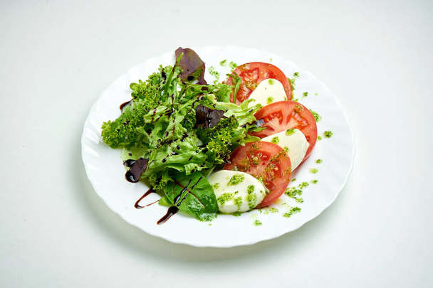 Classic Italian caprese salad with tomatoes, mozzarella, mix salad and pesto sauce in a white plate on a white plate - 写真・画像