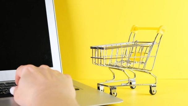 shopping basket next to a laptop on a yellow background. Copy space. Online shopping concept. - Photo, Image