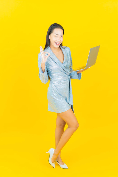 Portré gyönyörű fiatal ázsiai nő mosoly számítógép laptop sárga elszigetelt háttér - Fotó, kép