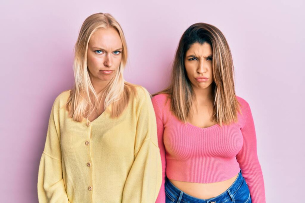 Zwei Freunde, die zusammen vor rosa Hintergrund stehen, sind skeptisch und nervös und runzeln ob des Problems die Stirn. negative person.  - Foto, Bild