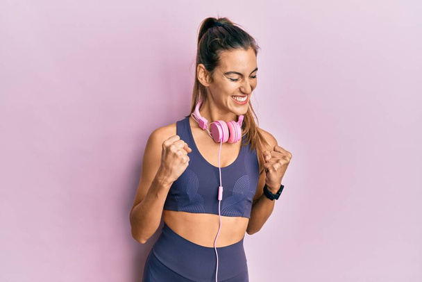 Young beautiful woman wearing gym clothes and using headphones excited for success with arms raised and eyes closed celebrating victory smiling. winner concept.  - Photo, Image