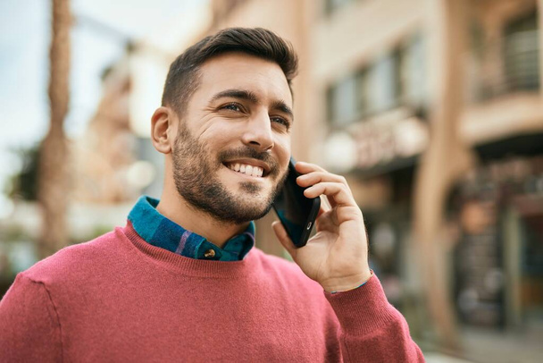 Junger hispanischer Mann lächelt fröhlich auf dem Smartphone in der Stadt. - Foto, Bild