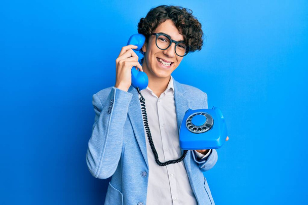 Hispanic young man speaking on vintage telephone smiling with a happy and cool smile on face. showing teeth.  - Photo, Image