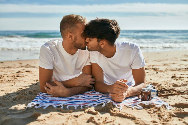 Young gay couple kissing lying on the sand at the beach. - Photo, Image