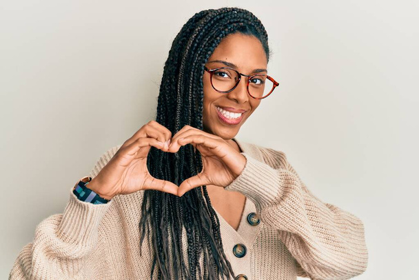 Afro-Amerikaanse vrouw draagt casual kleding en een bril glimlachend in liefde doen hart symbool vorm met handen. romantisch concept.  - Foto, afbeelding