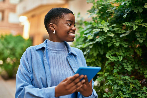 Jovem afro-americana sorrindo feliz usando touchpad na cidade - Foto, Imagem