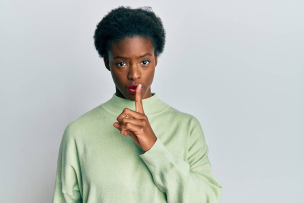 Jeune fille afro-américaine portant des vêtements décontractés demandant à se taire avec le doigt sur les lèvres. silence et concept secret.  - Photo, image