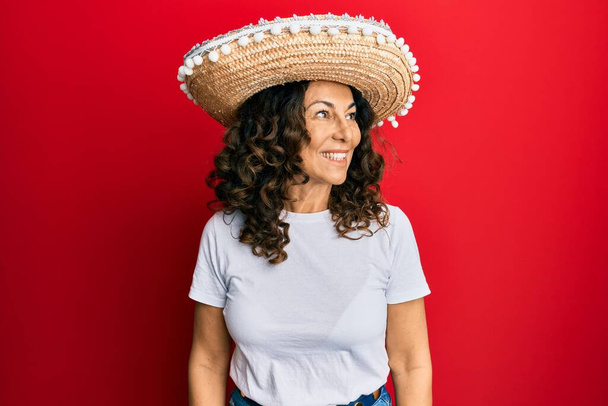 Keski-ikä latino nainen tilalla meksikolainen hattu katselee sivuun hymyillen kasvot, luonnollinen ilme. nauraen luottavainen.  - Valokuva, kuva
