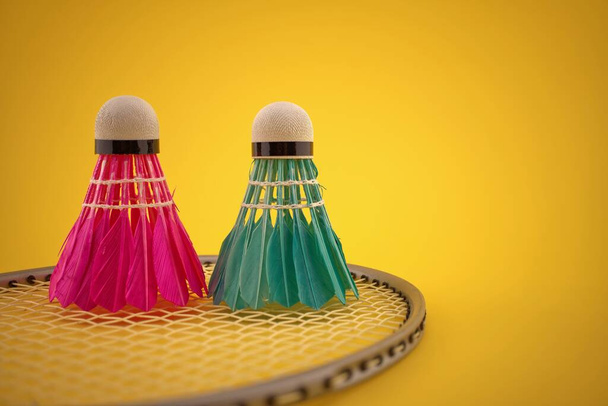 Badminton veer shuttlecocks op badminton racket over een gele achtergrond met kopieerruimte - Foto, afbeelding