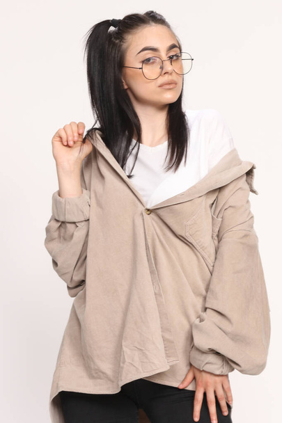 Beautiful caucasian hipster girl with black hair and glasses is posing in studio on isolated background. Style, trends, fashion concept. - Foto, immagini