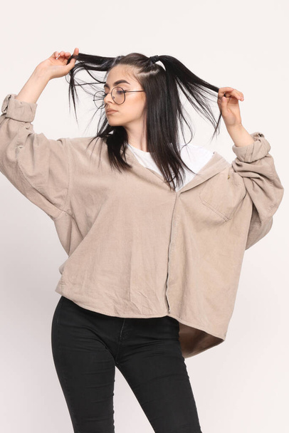 Gyönyörű fehér hipszter lány fekete hajjal és szemüveggel pózol a stúdióban, elszigetelt háttérrel. Stílus, trendek, divat koncepció. - Fotó, kép
