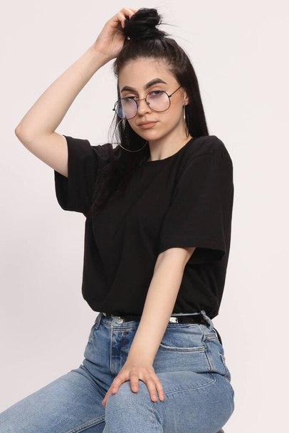 Beautiful caucasian hipster girl with black hair and glasses is posing in studio on isolated background. Style, trends, fashion concept. - Zdjęcie, obraz