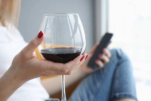 Vrouwelijke hand houdt glas wijn en smartphone - Foto, afbeelding
