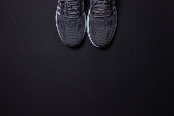 Серые кроссовки на черном фоне. Спортивная обувь. Понятие здорового образа жизни - Фото, изображение