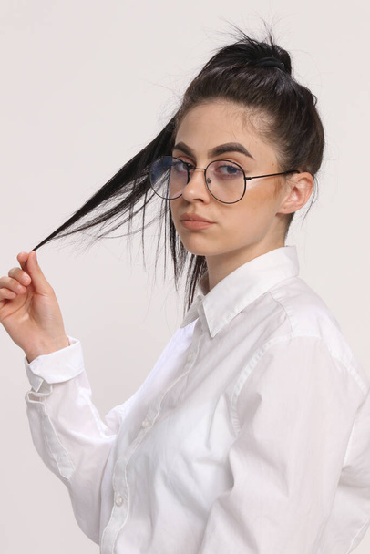 Prachtig Kaukasisch hipster meisje met zwart haar en bril poseert in studio op geïsoleerde achtergrond. Stijl, trends, modeconcept. - Foto, afbeelding