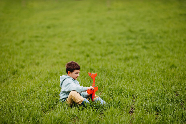 Poika leikkii punaisella lentokoneella, istuu pellolla vihreällä ruoholla. - Valokuva, kuva