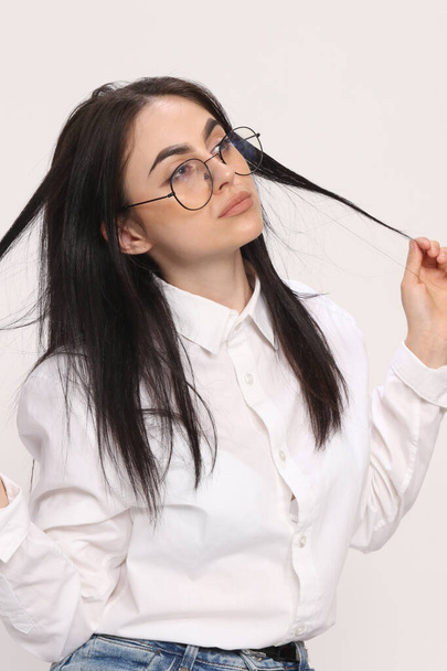 Bella ragazza hipster caucasico con i capelli neri e occhiali è in posa in studio su sfondo isolato. Stile, tendenze, concetto di moda. - Foto, immagini