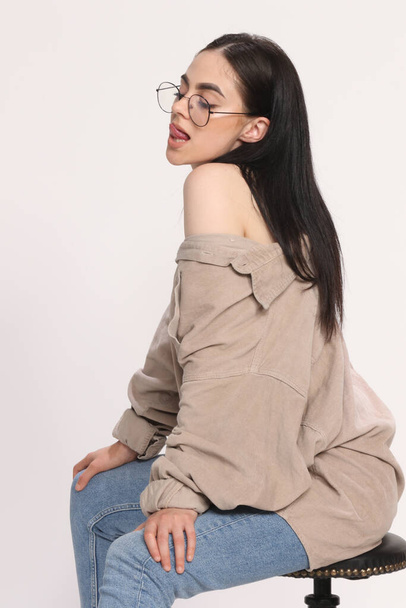 Prachtig Kaukasisch hipster meisje met zwart haar en bril poseert in studio op geïsoleerde achtergrond. Stijl, trends, modeconcept. - Foto, afbeelding