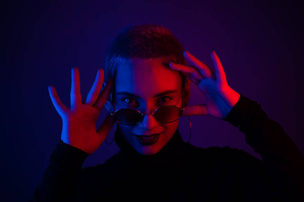 Portrait of a beautiful young woman with short hair in sunglasses in neon light - Foto, immagini