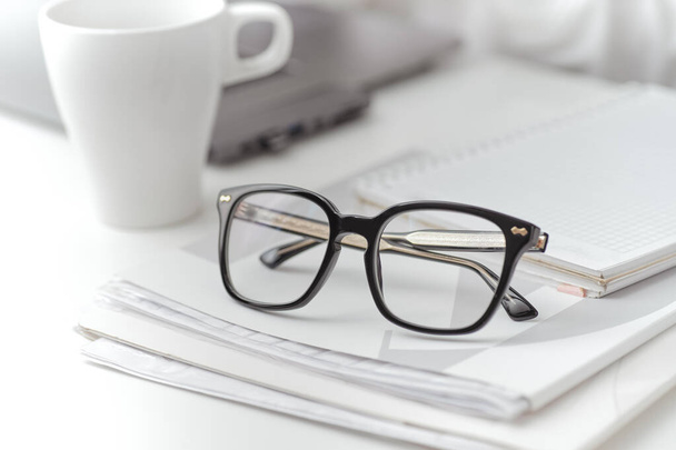 Nahaufnahme einer schwarzen Brille auf einem Ordner mit Dokumenten auf dem Schreibtisch. Eine Frauenarbeit im Hintergrund. Nahaufnahme - Foto, Bild