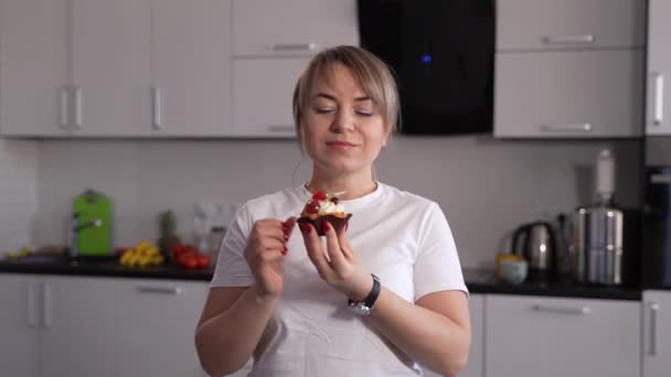 Happy female eating cherry from cake in kitchen - Footage, Video