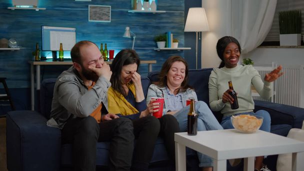 Felices amigos multiétnicos sonriendo juntos mientras están sentados en la helada de la televisión - Foto, Imagen