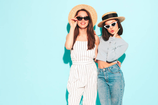 Three young beautiful smiling hipster female in trendy summer clothes. Sexy carefree women posing near light blue wall in studio. Cheerful and positive models in hats - Foto, immagini