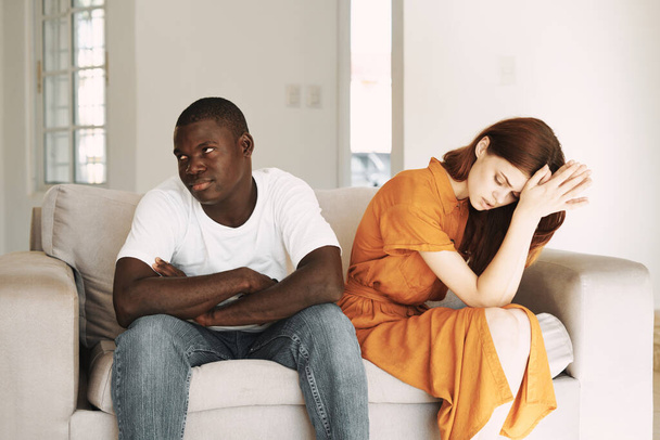 quarreled man and woman sitting on sofa indoors guy african appearance model - Foto, afbeelding